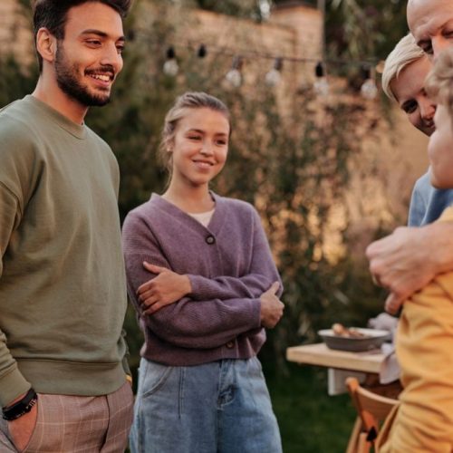 Group of cheerful multiracial relatives smiling and communicating in yard during meeting in summer weekends