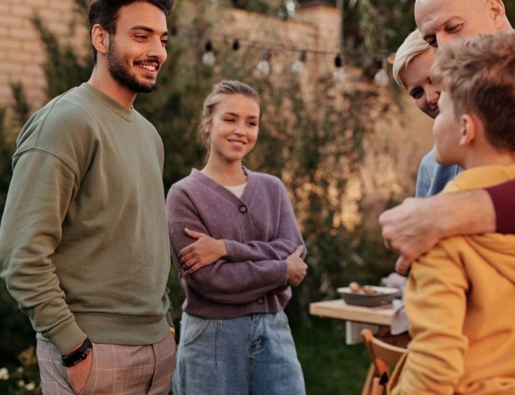 Group of cheerful multiracial relatives smiling and communicating in yard during meeting in summer weekends
