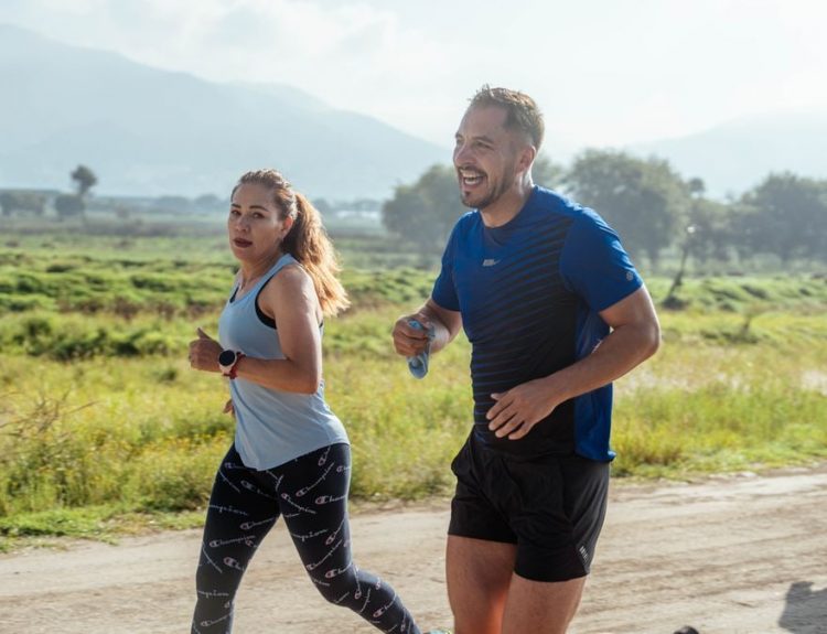 Two adults running on a rural dirt path, enjoying a sunny day outdoors.